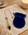 Black stone pendulum with lotus charm and blue velvet pouch on linen